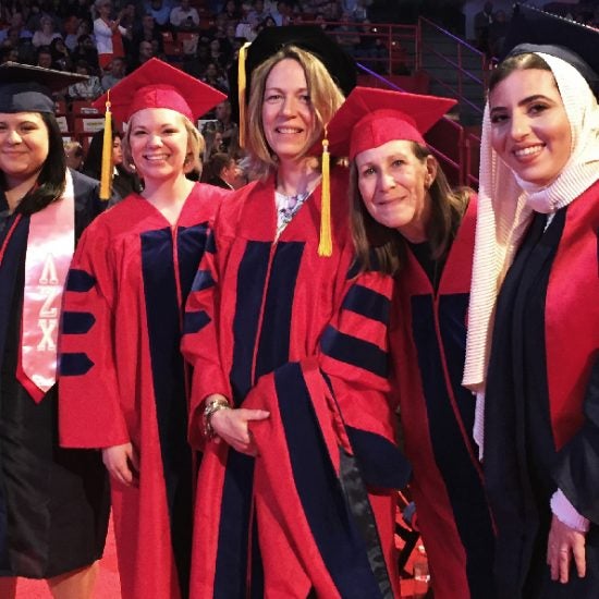 Three graduates in red and blue cap and gowns at commencement