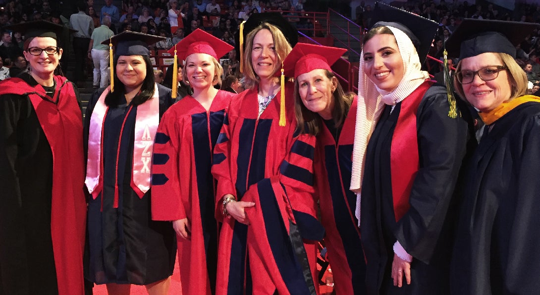 A group of faculty and graduates in their cap and gowns together at commencement