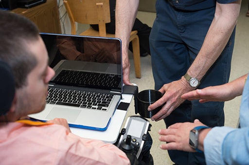 ATU staff work with an individual to modify a water bottle holder for a wheelchair