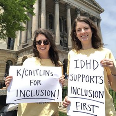 Kaitlin and Caitlin holding signs in front of building